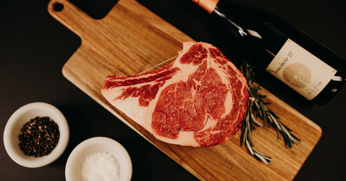 prime rib on cutting board next to bottle of red wine, salt and pepper