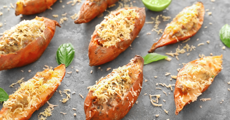 gray backdrop with multiple stuffed sweet potatoes topped with cheese, basil and limes