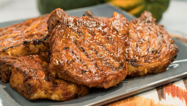 pumpkin bbq pork chops stacked on top of each other on a black cutting board