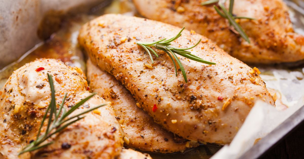 stack of seasoned chicken breasts topped with small sprigs of rosemary