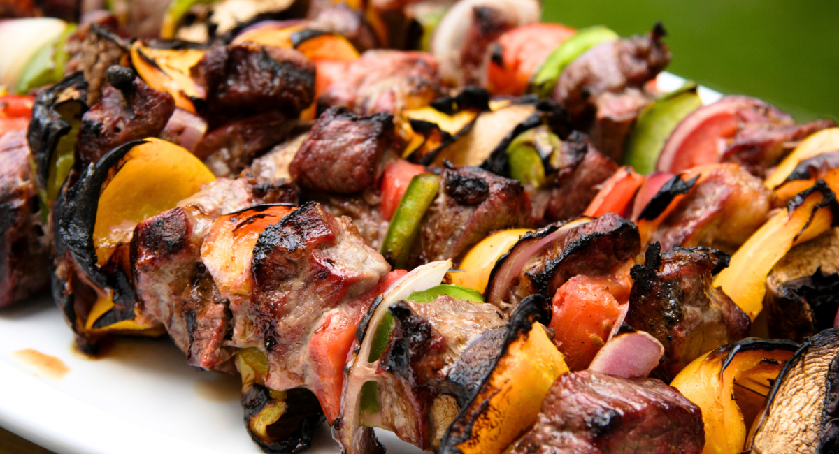 plate of marinated meats - four beef kabobs on a white plate with peppers and onions