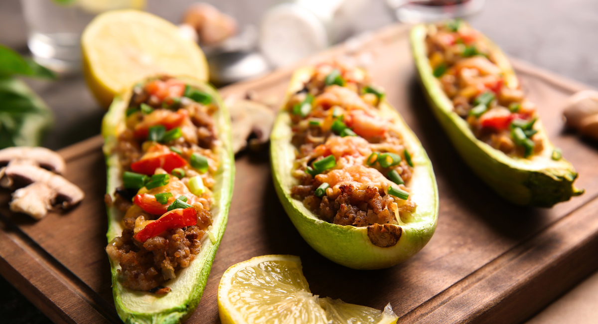 ground beef zucchini boats - three half-zucchinis on a cutting board filled with ground beef, red sauce, peppers and chives