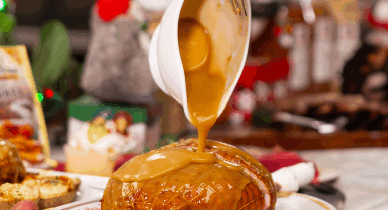 gravy in a white gravy bowl being poured over a smoked turkey breast that is cut in half