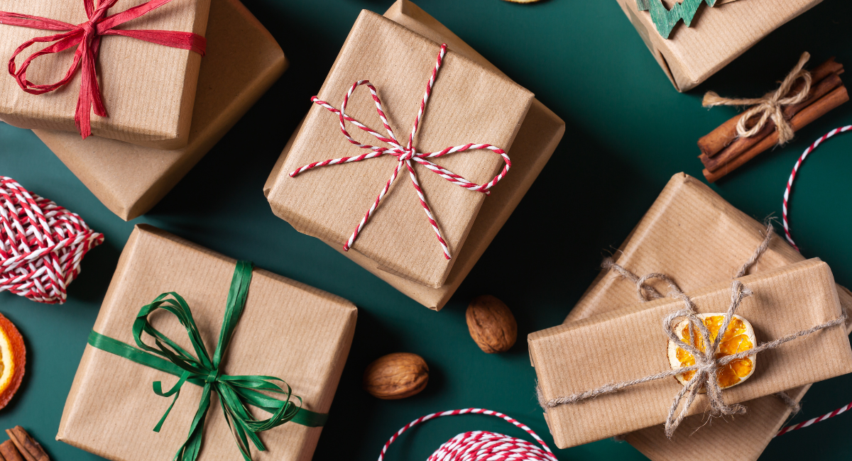 gartner's holiday gift guide - this photo features 8 presents wrapped in tan wrapping paper, featuring a variety of different ribbons. the gifts are laying on a green backdrop and surrounded by walnuts, dried fruit and cinnamon sticks