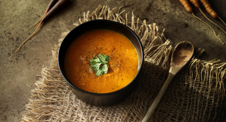 tortilla soup in a black bowl on a tan table cloth with a wooden spoon next to it