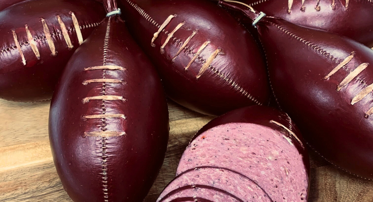 Six Gartner's football-shaped beef sticks on a wooden cutting board. One is sliced in half