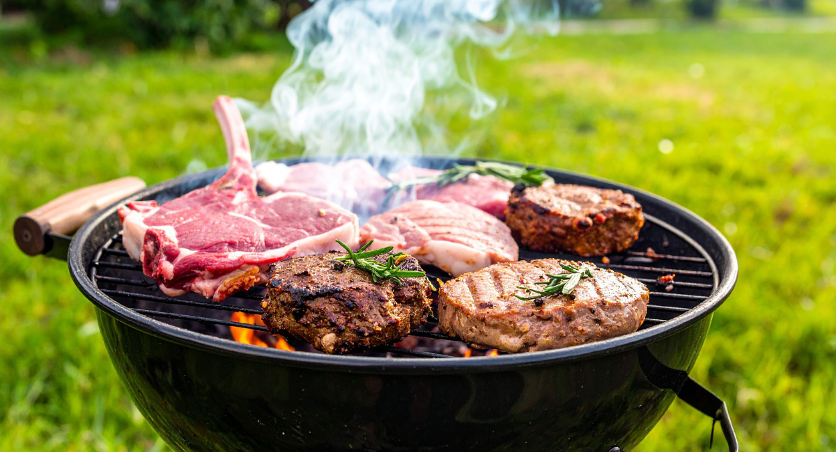 spring grilling - multiple steaks on a round grill situated on a grass lawn