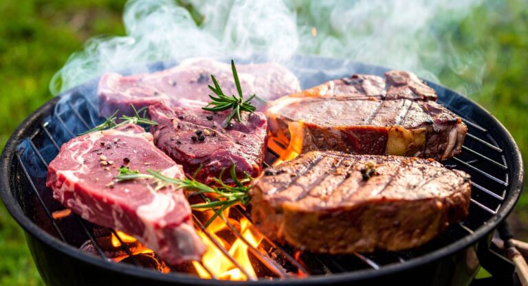 summer bbq - 5 steaks on a grill, two are more cooked than the other three. they are topped with peppercorns and rosemary sprigs on a charcoal grill.