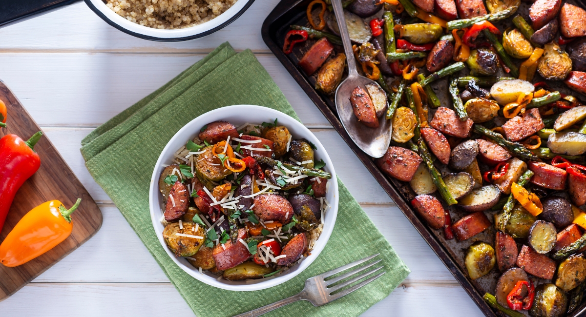 sheet pan vegetables and sausage - peppers, brussels sprouts, asparagus and more on a dish with a bowl of the same mixture to the side