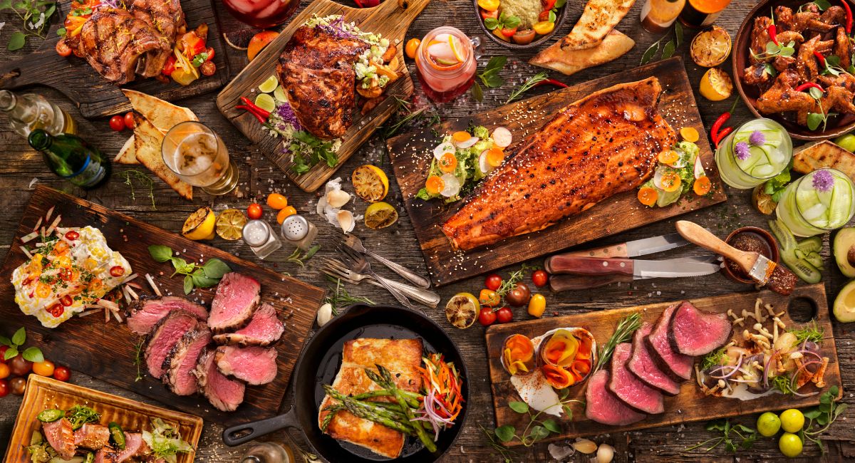 fall grilling set up - huge table filled with grilled salmon, fish, red meats. there are knives, forks and vegetables strewn throughout